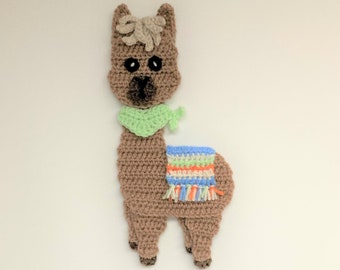 May include: A crocheted llama in shades of brown, tan, and black, with a green scarf and a colorful blanket. The handmade alpaca has black eyes and a detailed design, perfect for a nursery or as a unique gift.