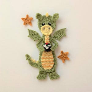 May include: A green crocheted dragon holding a red and white crocheted cupcake. The dragon has yellow stripes on its body and is surrounded by three orange crocheted stars.