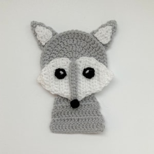 May include: A gray crocheted fox with white accents and black eyes. The fox is a flat, two-dimensional design.