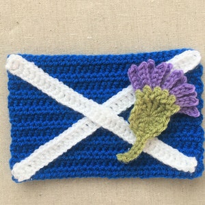 May include: Crocheted Scottish flag with a white X on a blue background and a purple and green thistle flower.