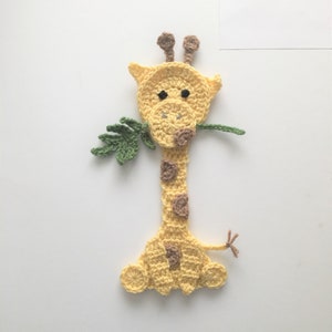 May include: A crocheted giraffe bookmark with a yellow body, brown spots, and green leaves in its mouth.