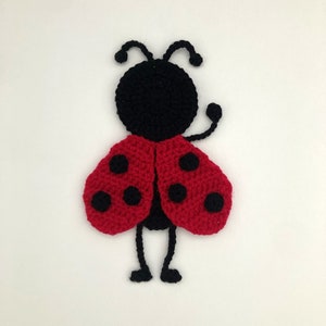 May include: A crocheted ladybug with red wings and black spots. The ladybug has black legs and antennae.