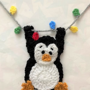 K&ouml;nnte beinhalten: Ein geh&auml;keltes Pinguin-Ornament, das an einer Schnur mit bunten Lichtern h&auml;ngt. Der Pinguin ist schwarz und wei&szlig; mit orangefarbenen F&uuml;&szlig;en und einem gelben Schnabel. Die Lichter sind rot, gr&uuml;n, blau und gelb.