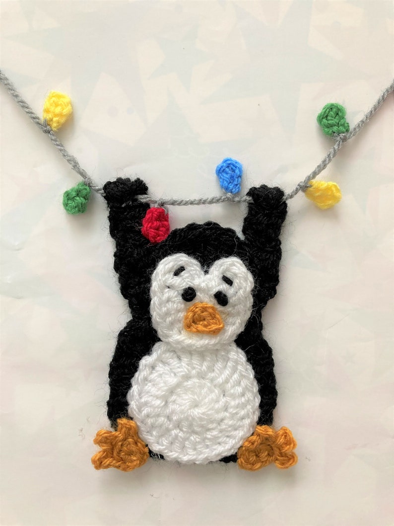 K&ouml;nnte beinhalten: Ein geh&auml;keltes Pinguin-Ornament, das an einer Schnur mit bunten Lichtern h&auml;ngt. Der Pinguin ist schwarz und wei&szlig; mit orangefarbenen F&uuml;&szlig;en und einem gelben Schnabel. Die Lichter sind rot, gr&uuml;n, blau und gelb.