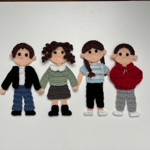 Könnte beinhalten: Vier handgefertigte Häkelpuppen sind abgebildet. Jede Puppe hat ein hellbraunes Gesicht und braune Haare und trägt verschiedene Outfits. Die Outfits umfassen eine schwarze Jacke, blaue Jeans, einen grünen Pullover, einen Rock, ein blaues Hemd, eine schwarze Hose und einen roten Kapuzenpullover.