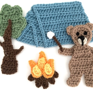 Puede incluir: Conjunto de aplicaciones de fieltro de crochet que incluye una tienda de campaña azul, un oso marrón que sostiene un palo con un malvavisco, un árbol verde, un tronco de árbol marrón y una fogata naranja y marrón.
