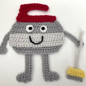 May include: A grey crocheted character with a red hat and a yellow crocheted broom. The character has a smiling face with black eyes and a black mouth.