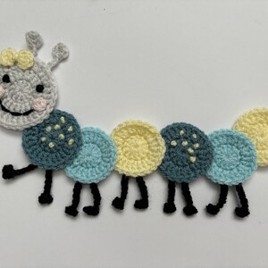 Peut inclure: Une chenille en crochet avec un visage souriant, des antennes jaunes et des segments de corps jaunes et bleus. La chenille a des pattes noires.