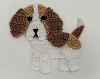 Puede incluir: Aplicación de perro de ganchillo en blanco, marrón y beige. El perro tiene orejas marrones, una cara beige y blanca y un cuerpo blanco. La cola del perro es beige y blanca. La aplicación está hecha de hilo.