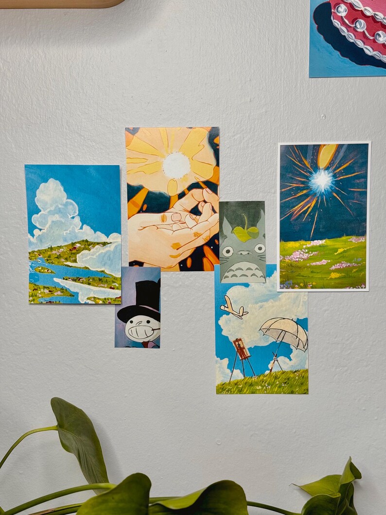 May include: A collection of colorful art prints featuring various scenes. One print depicts a blue sky with clouds and a landscape. Another shows a hand holding a bright light. Other prints include a cartoon character and a field with a bright light.