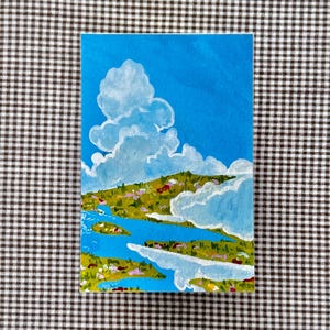 May include: A rectangular painting depicts a landscape with a bright blue sky and fluffy white clouds. Below, a green and yellow landscape is bisected by a blue river. The artwork is on a white background.