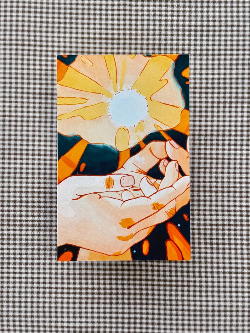 May include: A rectangular art print featuring a stylized illustration of two hands reaching towards a large, yellow flower with a light blue center. The background is dark blue with orange accents. The artwork is on a checkered surface.