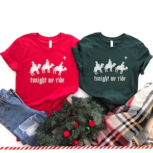 May include: Two Christmas themed t-shirts with a white graphic of the three wise men riding camels and the text "tonight we ride". One shirt is red and the other is green.