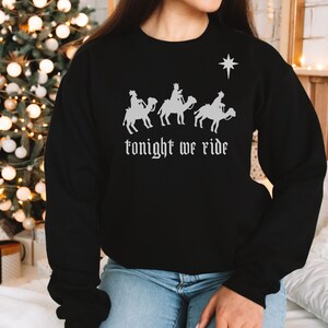 May include: Black sweatshirt featuring a graphic of three figures on camels, a star, and the text "tonight we ride" in white. The sweatshirt is a crew neck style, perfect for the holiday season.