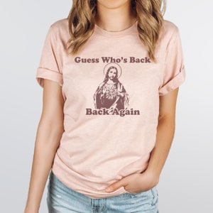 May include: A pink t-shirt with a graphic of Jesus and the text "Guess Who's Back Back Again".