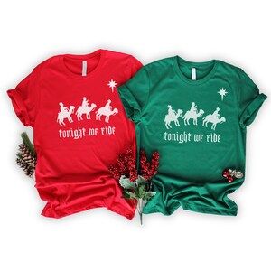 May include: Two Christmas themed t-shirts, one red and one green, with a white silhouette of three people riding camels and the text "tonight we ride".