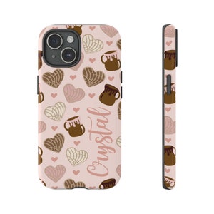 May include: A pink phone case with a pattern of brown and white heart-shaped pastries, brown clay pots with chocolate, and pink hearts. The text "Cristal" is written in pink on the case.
