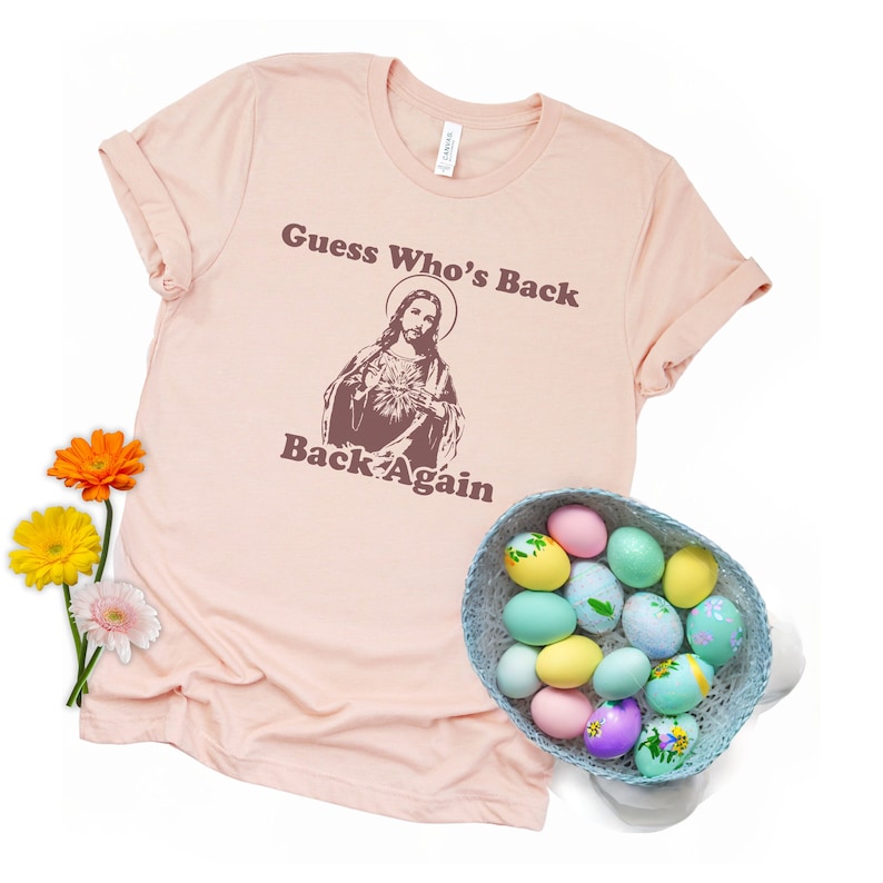 May include: A pink t-shirt with the text "Guess Who's Back Back Again" and an image of Jesus. The shirt is surrounded by Easter eggs in a basket.