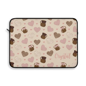 May include: A beige laptop sleeve with a pattern of brown and pink hearts, brown and pink concha shells, and the name "Crystal" in pink lettering.