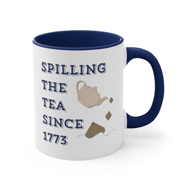 Op de afbeelding: Witte keramische mok met een marineblauwe binnenkant en handvat. De mok heeft de tekst "Spilling the Tea Since 1773" met een illustratie van een theepot en thee die eruit stroomt. Een leuk cadeau voor theeliefhebbers.