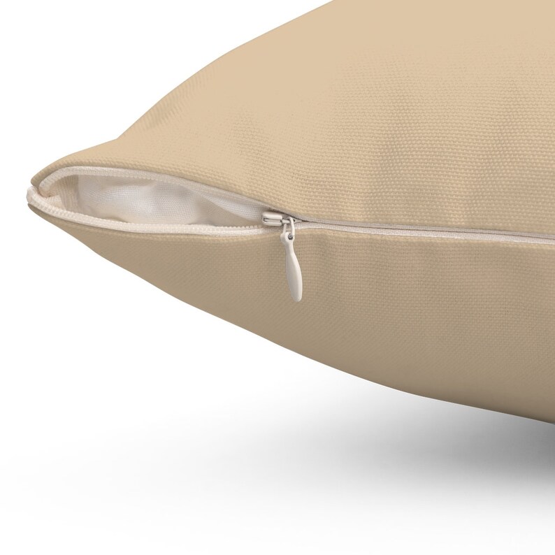 Puede incluir: Una almohada beige con cierre de cremallera. La cremallera es blanca y tiene un tirador.