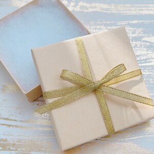 May include: A beige gift box with a gold ribbon tied in a bow. The box is open and the inside is lined with white tissue paper.