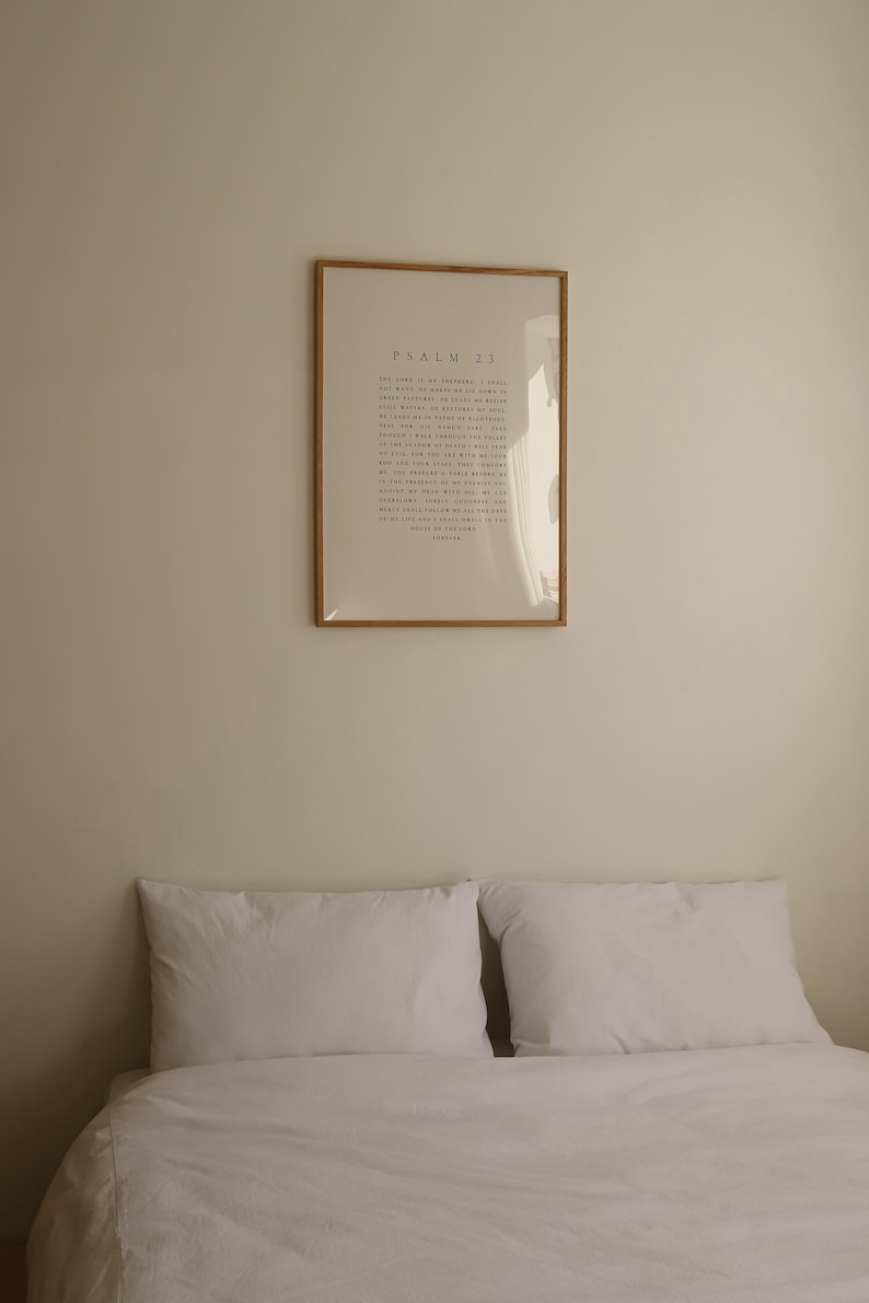 May include: A white bed with two white pillows and a framed print on the wall behind it. The print is a light beige color and has the text "PSALM 23" in black lettering.