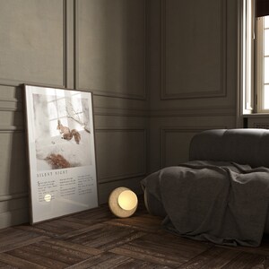May include: A framed print of a squirrel in a snowy forest with the text "Silent Night" and lyrics below the image. A round, gold-colored lamp sits on the wooden floor next to a gray couch.