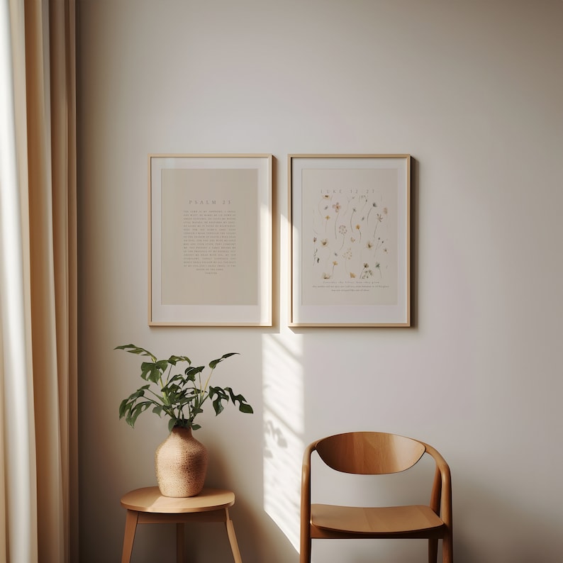 May include: Two framed prints on a white wall. The print on the left has the text "PSALM 23" and the print on the right has the text "LUKE 12:27". A potted plant sits on a small wooden table in the corner of the room.