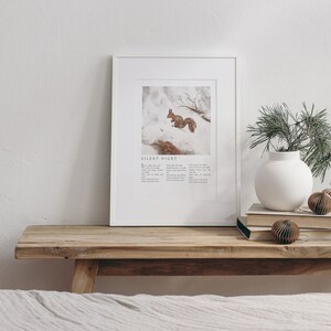 May include: A framed print with a white background and a picture of a squirrel in the snow. The print has the text "Silent Night" and the lyrics to the song printed below the image.