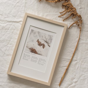 May include: A framed print with a watercolor illustration of a squirrel in a snowy forest. The print includes the lyrics to the Christmas carol "Silent Night".