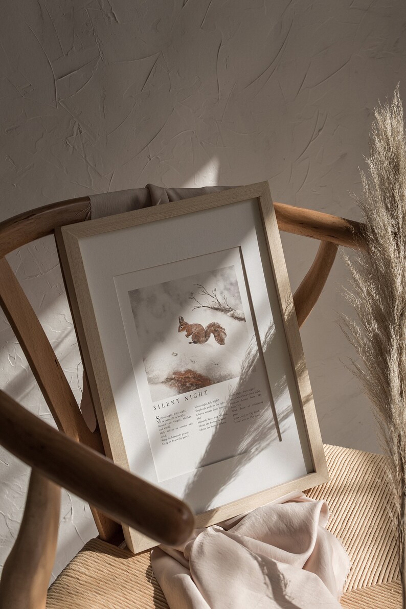 May include: A framed print with a watercolor illustration of a squirrel in a snowy forest. The print includes the lyrics to the Christmas carol "Silent Night".