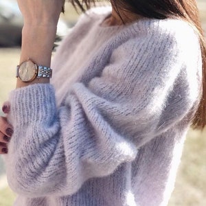 May include: A soft, light purple sweater with a loose fit and long sleeves. The sweater is made of a fuzzy, mohair-like yarn.