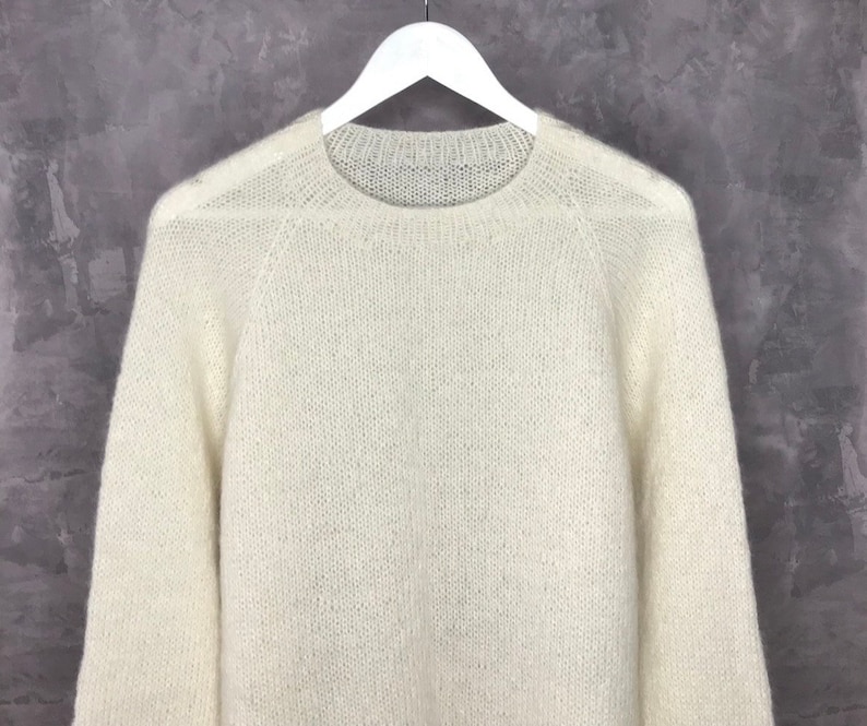May include: A white, fluffy knit sweater with a round neckline and long sleeves.