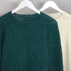 May include: Two sweaters, one green and one white, hanging on white hangers against a light gray background.