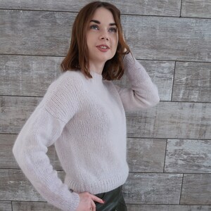 May include: A soft, light pink sweater with a round neckline and long sleeves. The sweater is made of a fine knit and has a slightly loose fit.