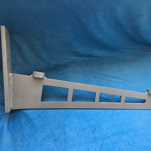 Puede incluir: Un soporte de estante de metal plateado con cuatro recortes rectangulares y dos agujeros redondos. El soporte está diseñado para montarse en una pared.