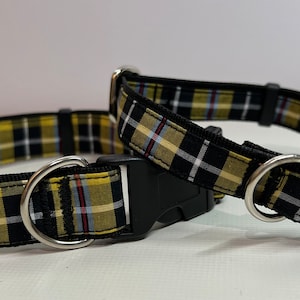 May include: Two dog collars featuring a black, yellow, and white tartan design. Each collar has a black plastic buckle and a silver metal D-ring for lead attachment. The collars are presented on a white surface.