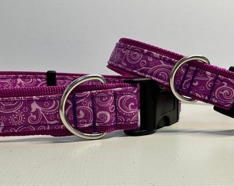 Puede incluir: Dos collares para perros de color morado con un patrón de espiral blanco. Los collares tienen anillas en D plateadas y hebillas de plástico negro.
