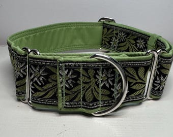 May include: A green dog collar with a floral pattern in black and olive green. The collar has a padded green interior and silver-colored metal hardware. The decorative fabric is woven with a detailed floral design.