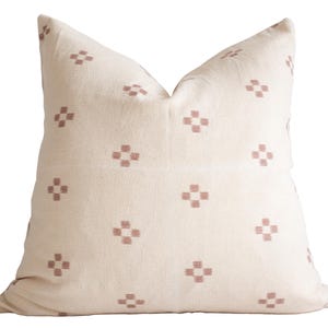 Puede incluir: Una almohada blanca con un patrón geométrico rosa. La almohada está hecha de una tela suave y tejida y tiene una forma cuadrada.