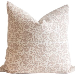 Puede incluir: Una almohada decorativa con un patrón floral en tonos beige y marrón. La almohada está hecha de una tela suave, similar al lino.