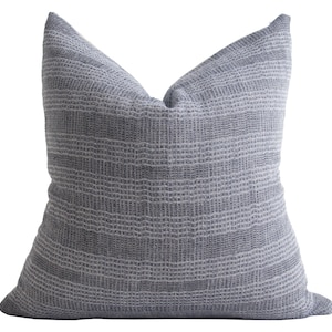 Puede incluir: Una almohada de tiro gris y blanca con textura tejida.