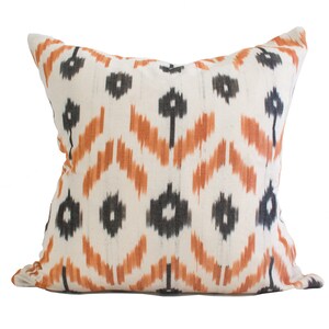 May include: A white cushion with a black and orange ikat pattern. The cushion is made of a soft, woven fabric and has a subtle sheen.