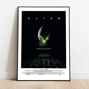 May include: Framed movie poster for the film "Alien." The poster features the title in white capital letters above an image of an egg with a glowing green interior. The tagline reads, "In space no one can hear you scream."