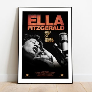 Puede incluir: Un póster enmarcado con Ella Fitzgerald. El póster tiene un fondo negro con el nombre "ELLA FITZGERALD" en letras naranjas en la parte superior. Debajo, el texto "JUST ONE OF THOSE THINGS". Una foto en blanco y negro de Fitzgerald cantando está en el centro.