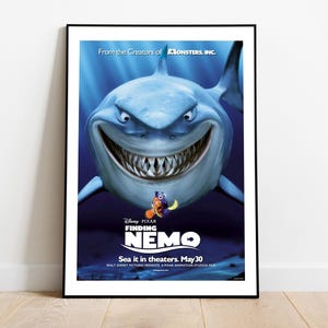 May include: Framed poster for the animated film "Finding Nemo." The poster features a large, menacing shark with sharp teeth, set against a blue underwater background. The film's title and release date are also displayed.