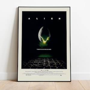 May include: Framed movie poster for the film "Alien." The poster has a dark background with a large egg shape and the title "Alien" in white letters. The tagline reads "In space no one can hear you scream."