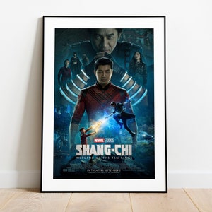 以下が含まれることがあります： 赤と黒の衣装を着た中心人物が描かれた、「シャン・チー・アンド・ザ・レジェンド・オブ・ザ・テン・リングス」の額入り映画ポスター。ポスターは、いくつかのキャラクターとマーベル・スタジオのロゴが入った、濃い青とティール色の配色です。