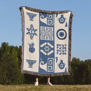 Könnte beinhalten: Eine blaue und weiße Wandteppich mit geometrischen Mustern und Symbolen, darunter ein stilisiertes Auge, eine Vase und eine Sonne. Der Wandteppich ist mit Fransen versehen und hat eine gewebte Textur.